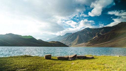 The Chandratal lake, over a background of tall mountains, under a cloudy, blue sky, Spiti, India