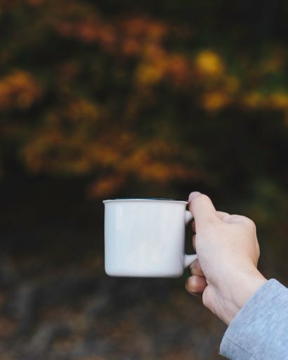 A selective focus of a hand holding a coffee mug on a autumn leaves background