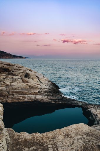 A vertical shot of purple sunset over the seascape and rocky cliffs on a coast