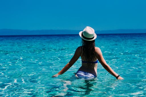 A back view of a young female with a hat in a blue ocean on a sunny summer day