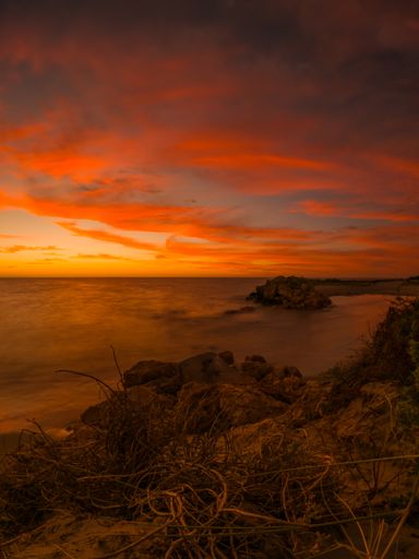 A beautiful scene of long exposure of grass rocks by the majestic water with Stunning orange sunset sky