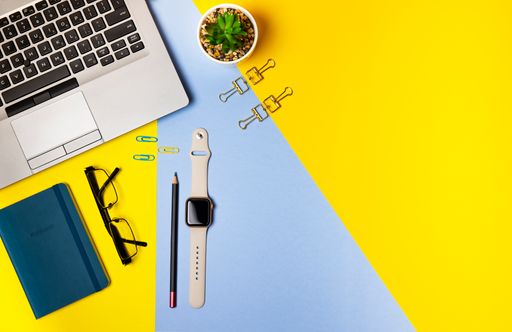 A Top view with copy space of a yellow office with laptop, glasses, pencil, blue note and a smartwatch