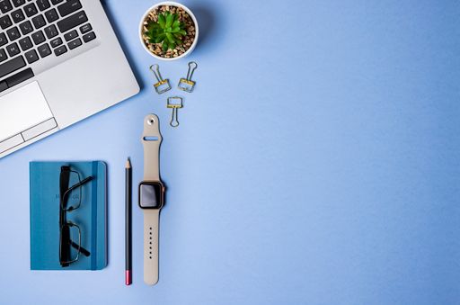 A Top view with copy space of a blue office with laptop, glasses, pencil, blue note and a smartwatch