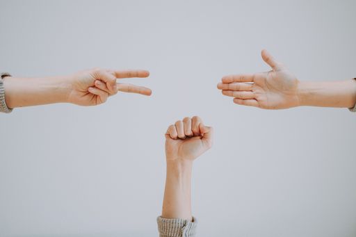 A wide shot of three people playing the game of rock paper scissors on a gray background