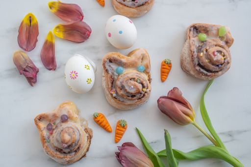 A top view shot of Cinnamon rolls, Garden tulip and decorated easter eggs on a white background