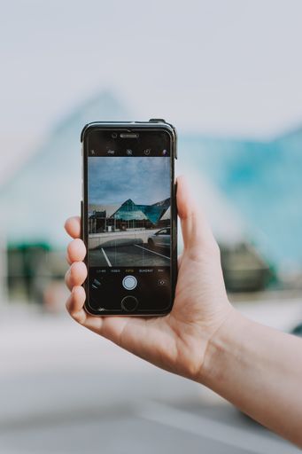 A vertical selective shot of a person holding black phone taking a picture of triangular architectural building