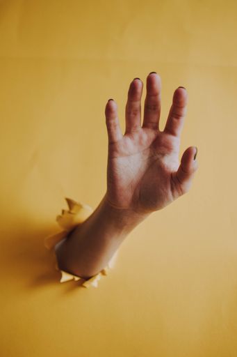 A vertical shot of a hand coming out of a yellow wall hole with open palm