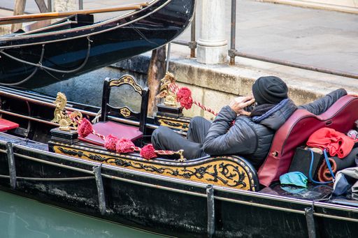 A Gondolier wearing a hat talking on his cell phone in a gondola in Venice Italy