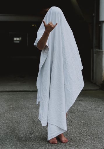 A vertical shot of a barefoot person wearing white ghost sheet showing shaka sign