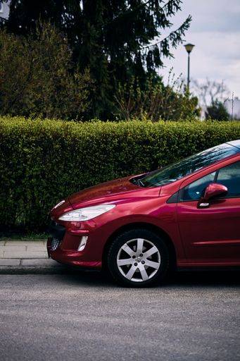 A vertical shot of a parked red Peugeot 308 car by a sidewalk.