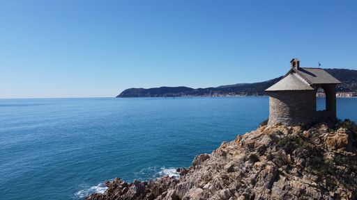 A scenic view of a clear sea and the rocky coastline of Alassio under the bright sky