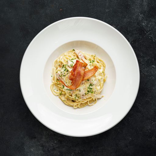 A top view of tasty carbonara pasta on a white plate
