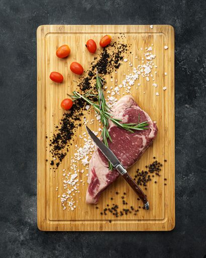A vertical top view of a piece of meat with ingredients on a cutting board