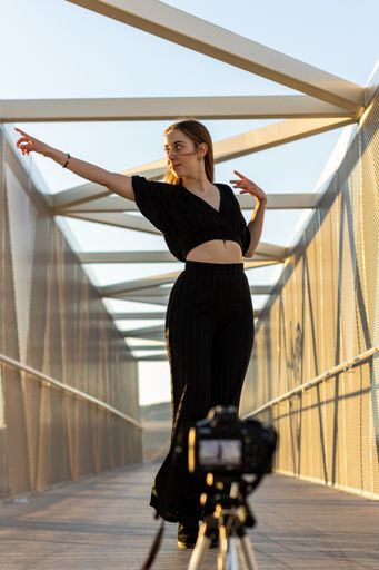 A vertical portrait of a young blonde Caucasian woman filming her dances on a camera outdoors