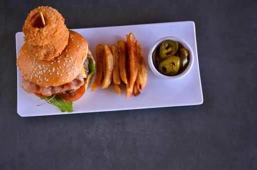 A top view of a hamburger, French fries, and slices of preserved Jalapeno pepper served on a white plate