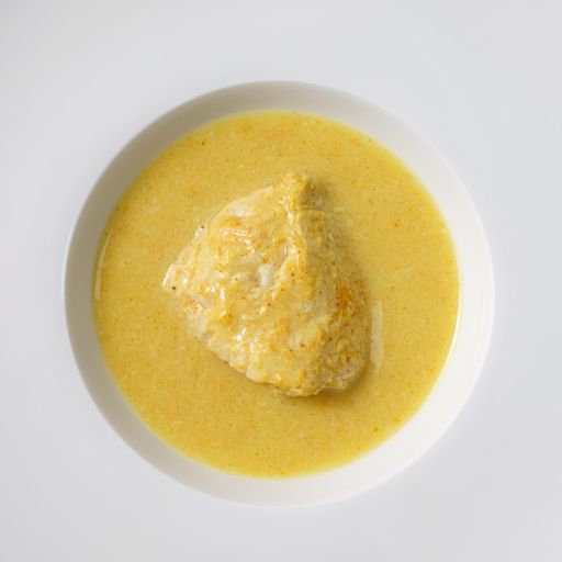 A closeup of a spicy chicken curry with coconut milk in a white plate