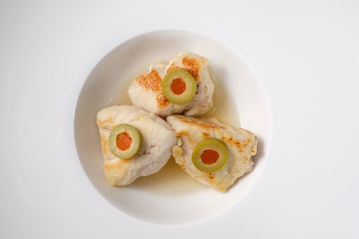 A closeup of chicken meat with green olives in a white bowl