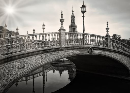 A beautiful shot of a bridge over the water with a lamp post in black and white