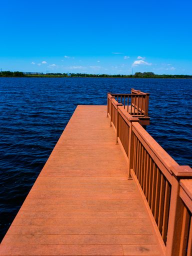 A vertical shot of a wooden pier colored in orange and the view of the blue water of the sea
