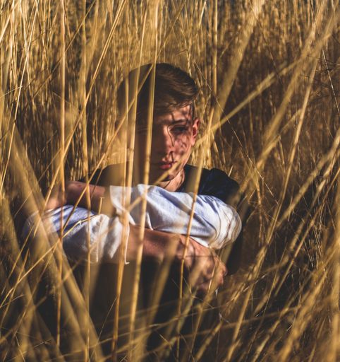 Photo of a kid sitting in a field of whey, dressed in a black and white shirt, and feeling very sad. This photo has very interesting shadows.
