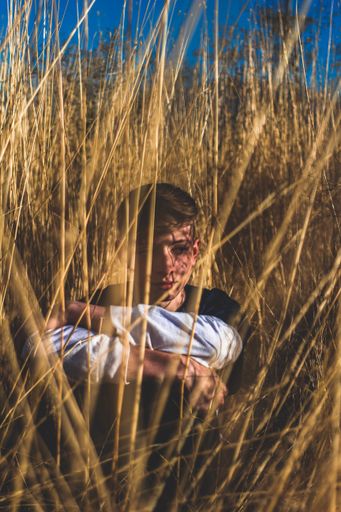 Photo of a teenager sitting in dry grass, dressed in a black and a white shirt. He has shadows in his face. The image was taken in Utah last year.
