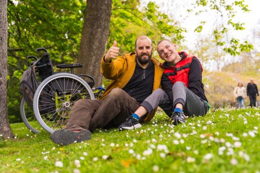 A view of a paralyzed young man with a friend sitting on the grass of a public park in the city
