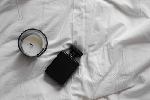 A top view of a candle and perfume on a white bedsheet