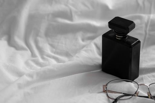 A black perfume bottle and glasses on a white bedsheet