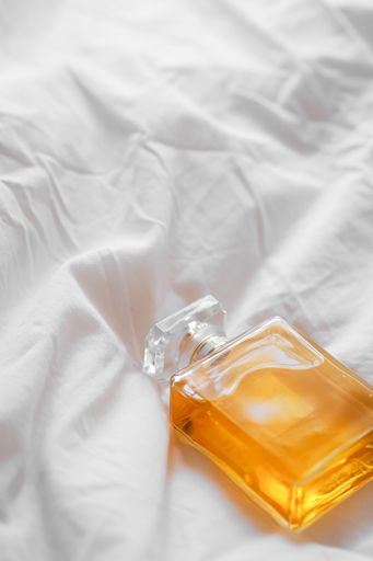 A vertical shot of a luxury perfume bottle on a white bedsheet