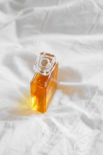 A top view of a transparent perfume bottle on a white sheet in bright light