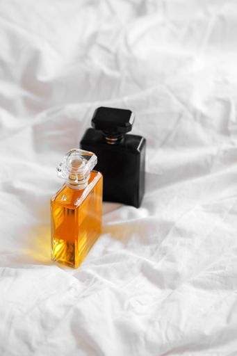 A vertical shot of two perfume bottles on a white bedsheet