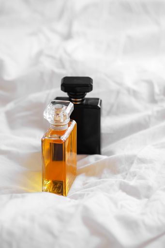 A vertical shot of two perfume bottles on a white bedsheet on a blurred background