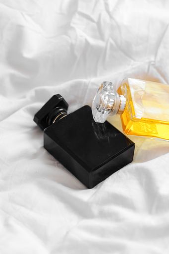A vertical shot of two perfume bottles on a white bedsheet