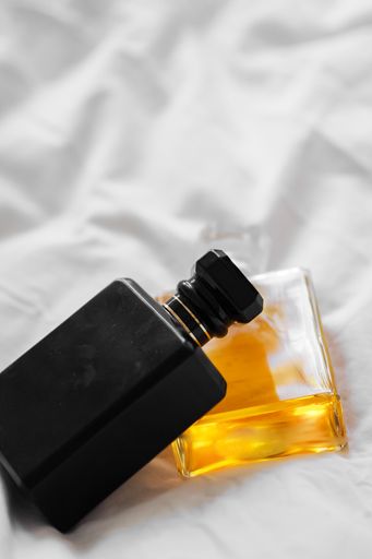 A vertical shot of two perfume bottles on a white bedsheet on a blurred background