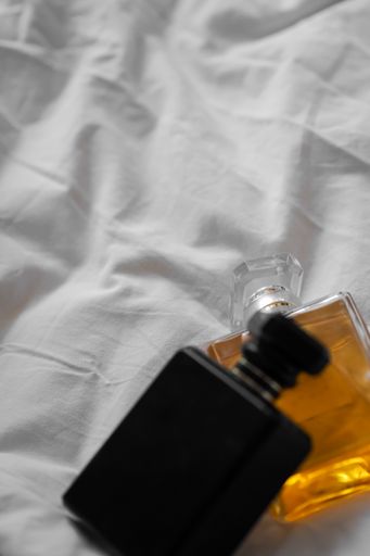 A vertical shot of two perfume bottles on a white bedsheet