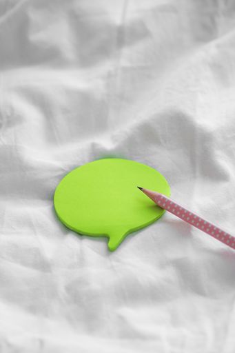 A vertical shot of a pencil and colorful bubble-shaped sticky papers on a white bedsheet