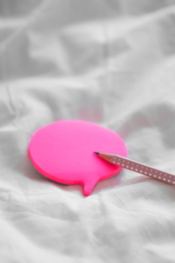 A vertical shot of a pencil and colorful bubble-shaped sticky papers on a white bedsheet