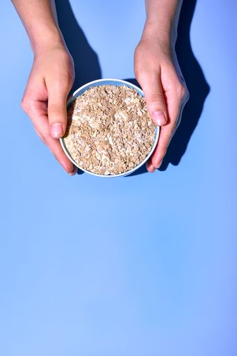 A person's hands holding a bowl of oat flakes on a blue background