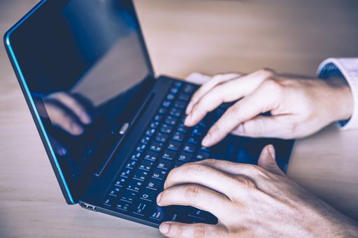 A closeup of a person's hands writing an e-mail on a laptop