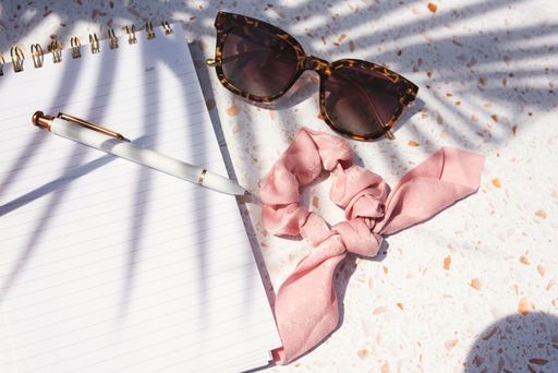 A top view of sunglasses and a scrunchie on a notebook in sunlight