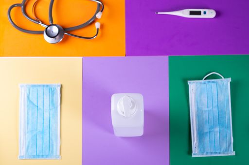 A high angle view of a bottle of hand sanitizer, facemasks, thermometer and a stethoscope on colorful papers - COVID-19