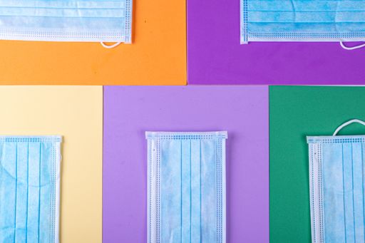 A high angle view of facemasks on colorful papers on the table - COVID-19