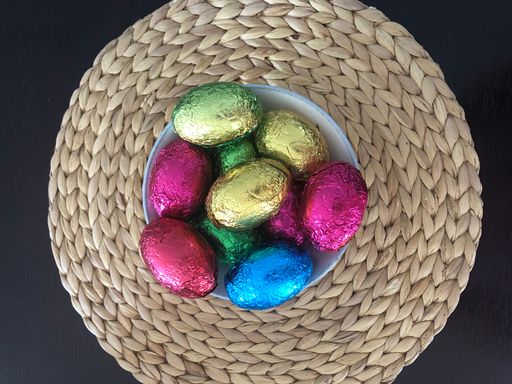 From above colourful foil wrapped chocolate easter eggs in a bowl on a straw wicker woven placemat from above overhead shiny bright colourful wrapping