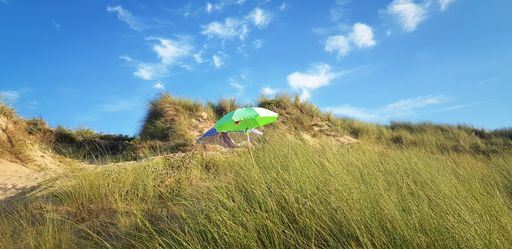 a panoramic shot of a yellow sun umbrella on hill against blue sky background