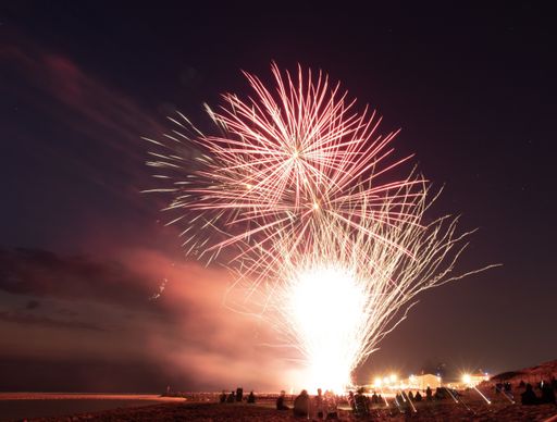 A beautiful horizontal shot of fireworks at night time with people celebrating under the colorful night sky