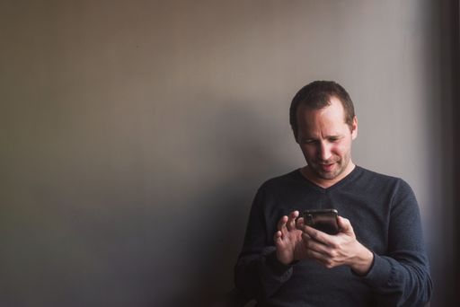 A closeup shot of a caucasian man sitting looking at his phone and smiling