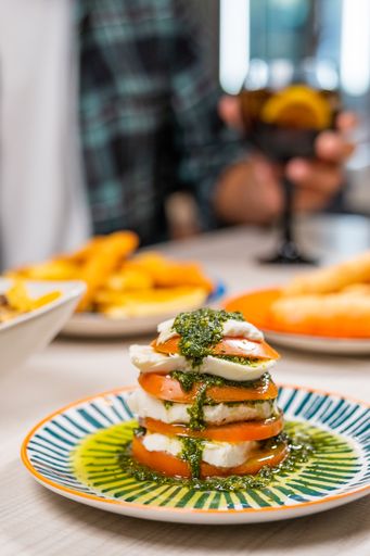 A vertical shot of caprese salad made of tomato, mozzarella, and pesto sauce, on a restaurant table