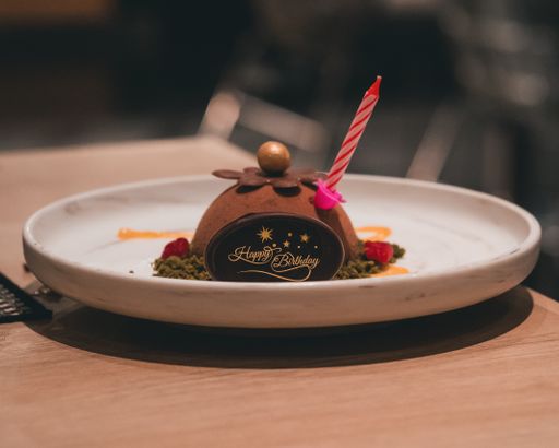 A closeup shot of a mini chocolate birthday cake saying "Happy Birthday" with a candle on top
