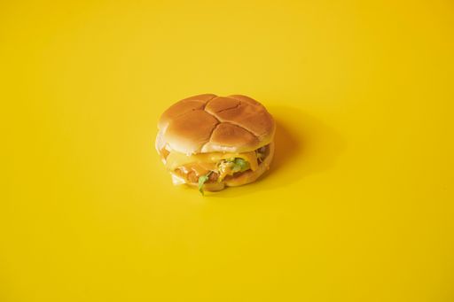 A closeup of a cheeseburger on a plain yellow background looking delicious and fresh