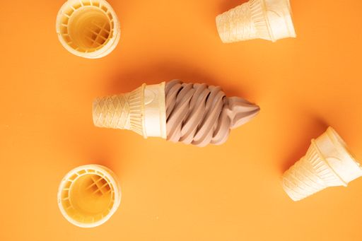 A top view of chocolate ice-cream and four waffle cones around it on an orange surface looking yummy